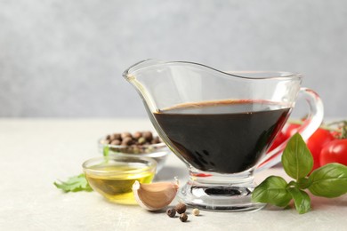 Photo of Balsamic vinegar in gravy boat, oil, basil and spices on gray textured table, space for text