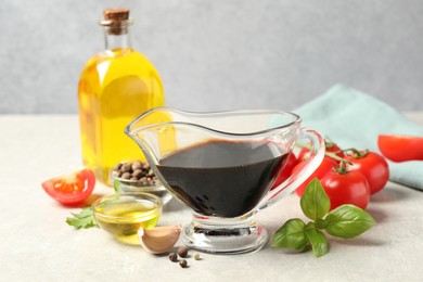 Photo of Balsamic vinegar in gravy boat, oil, tomatoes, herbs and spices on gray textured table