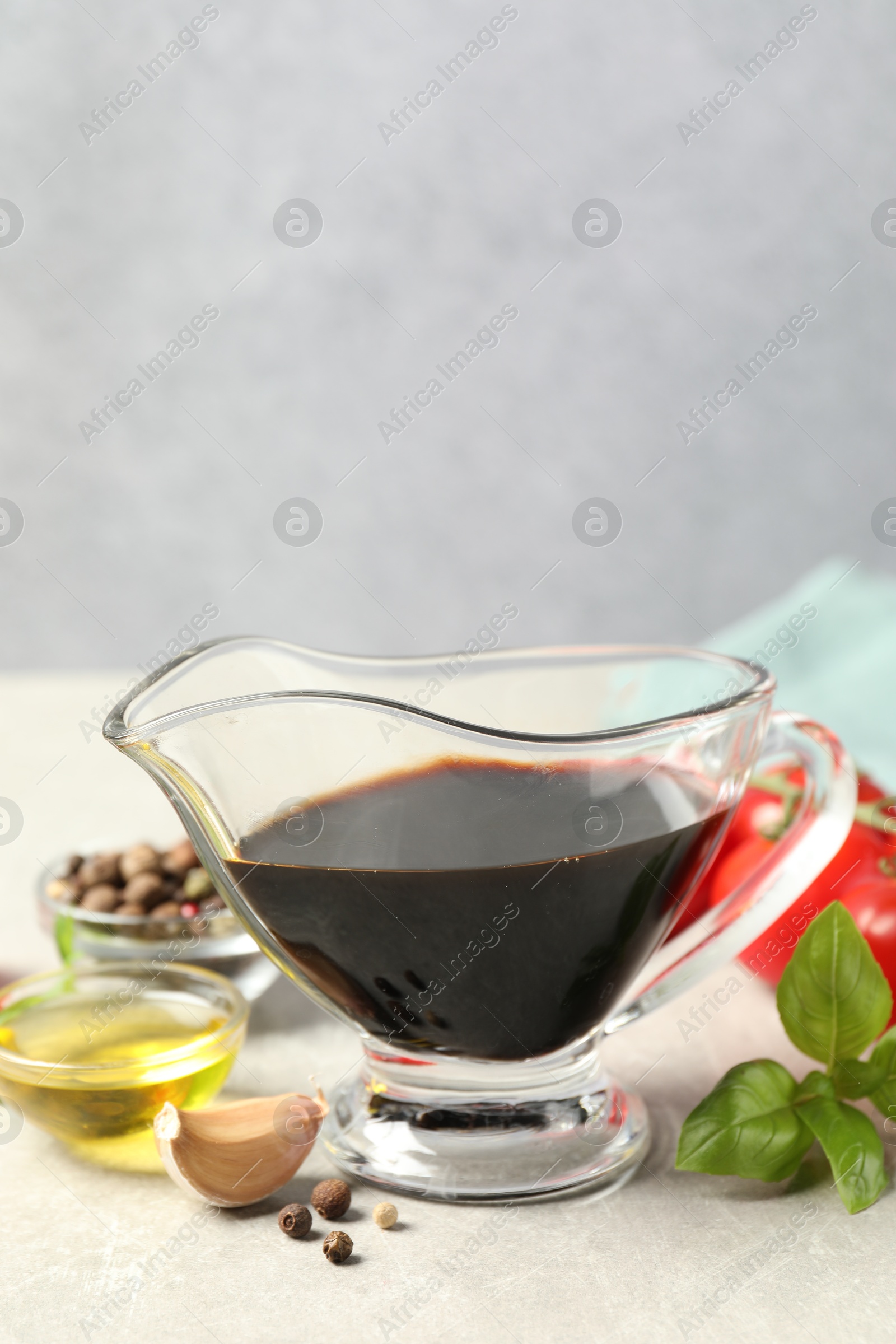 Photo of Balsamic vinegar in gravy boat, oil, basil and spices on gray textured table, space for text