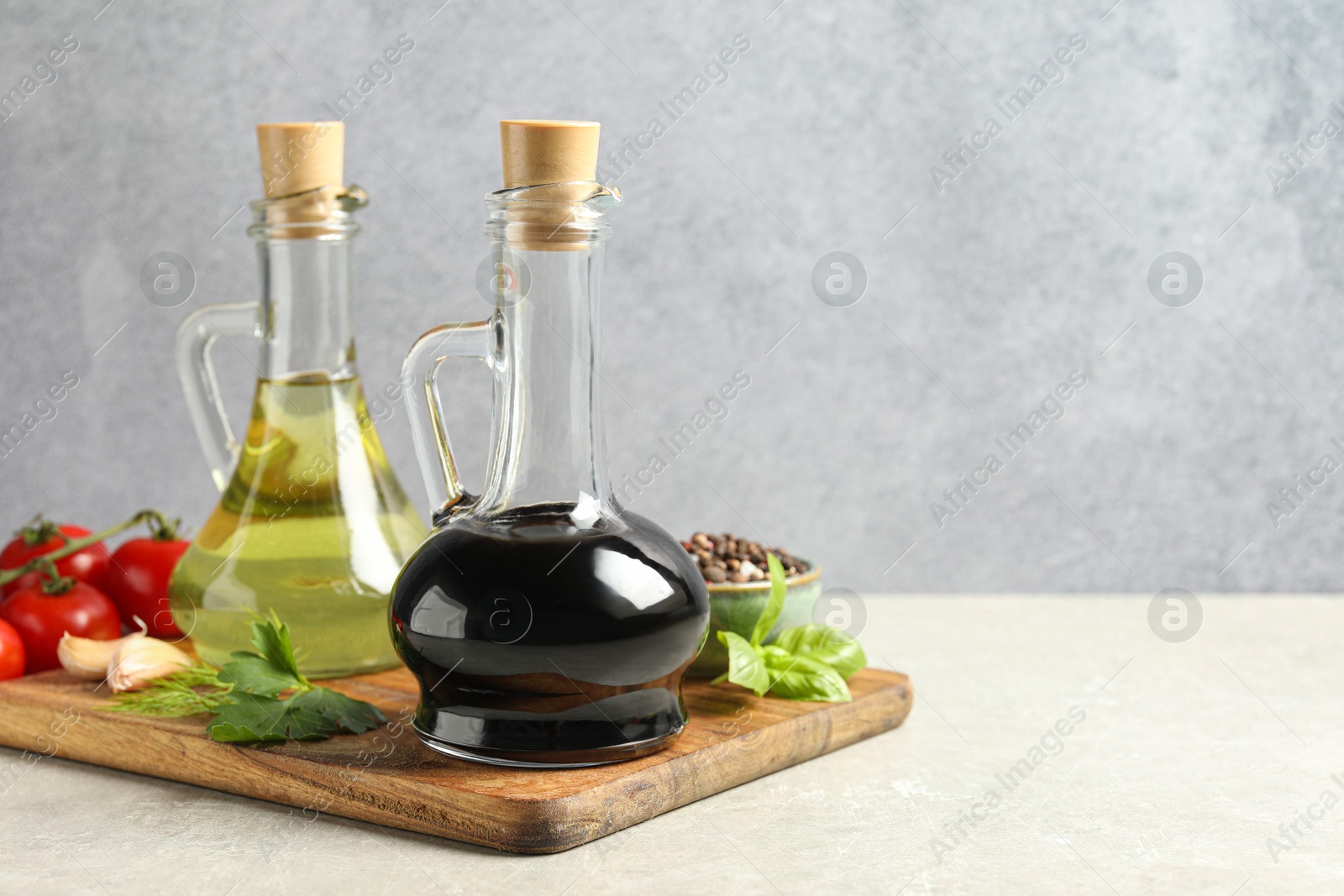 Photo of Balsamic vinegar in glass jug, oil, tomatoes, herbs and spices on gray textured table, space for text