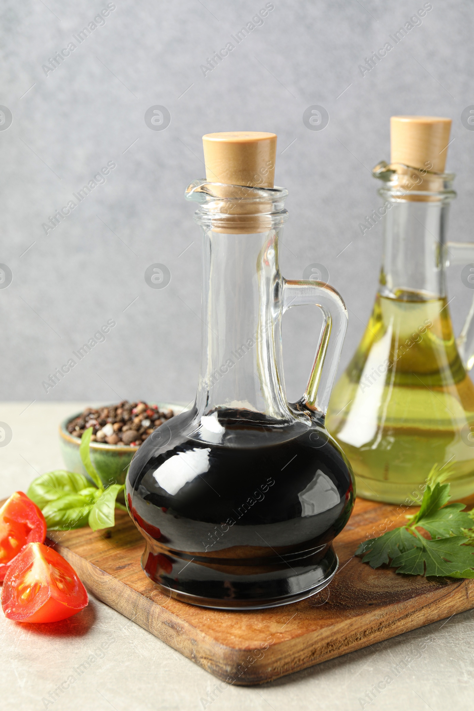 Photo of Balsamic vinegar in glass jug, oil, tomatoes, herbs and spices on gray textured table