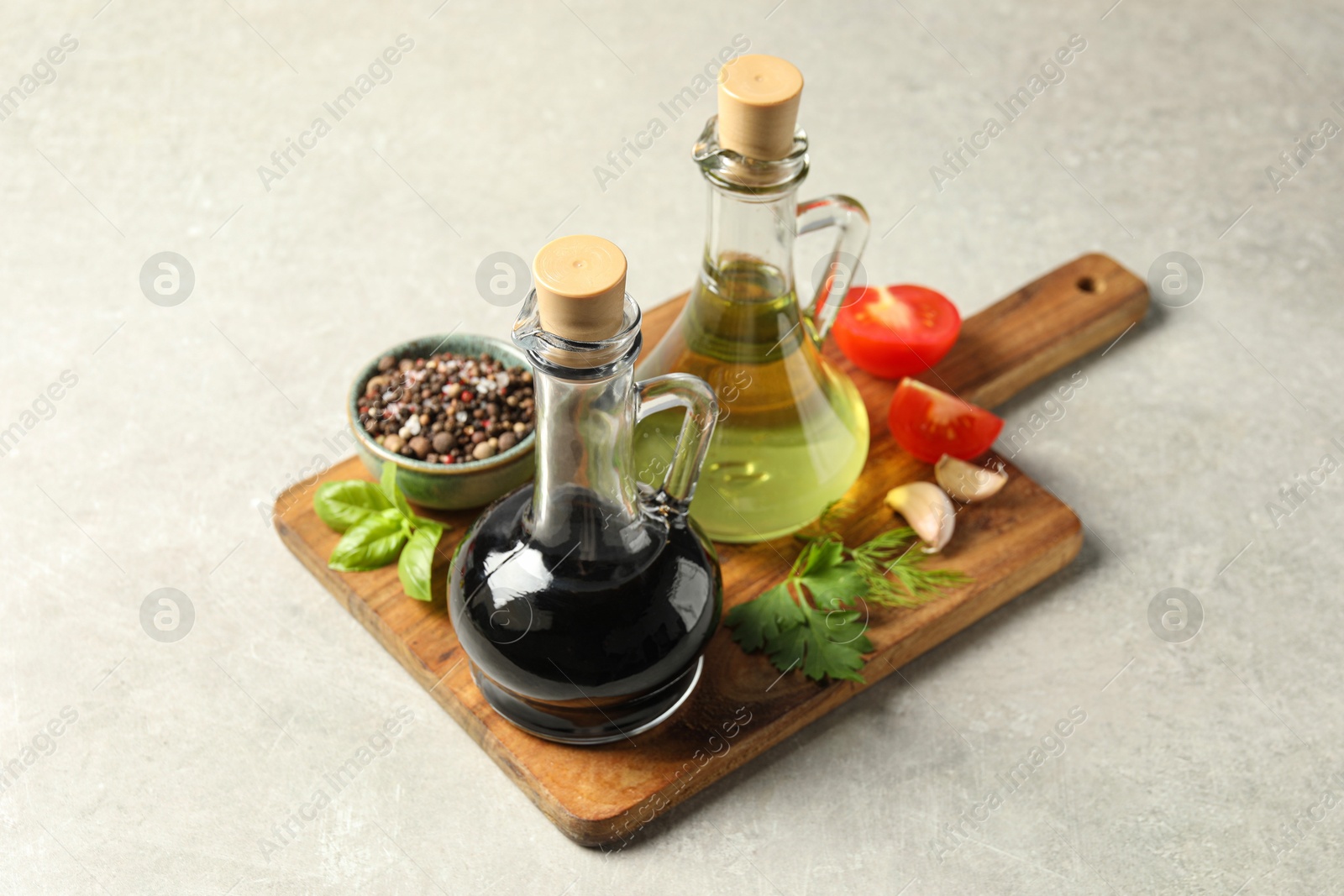 Photo of Balsamic vinegar in glass jug, oil, tomatoes, herbs and spices on gray textured table