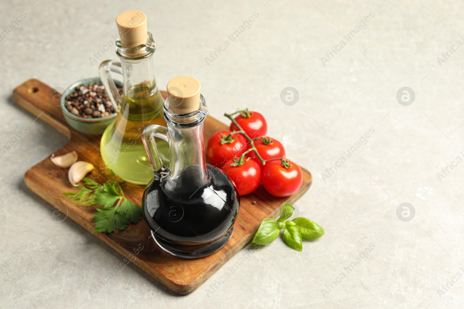 Photo of Balsamic vinegar in glass jug, oil, tomatoes, herbs and spices on gray textured table, space for text