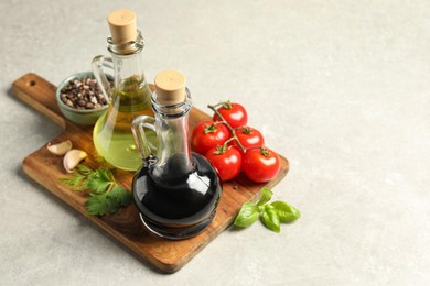 Balsamic vinegar in glass jug, oil, tomatoes, herbs and spices on gray textured table, space for text