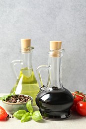 Photo of Balsamic vinegar in glass jug, oil, tomatoes, herbs and spices on gray textured table, closeup