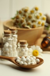 Photo of Homeopathic remedy. Spoon with pills, bottles and chamomile flowers on white table, closeup