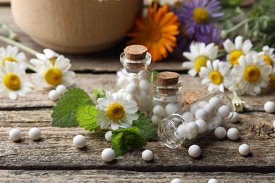 Homeopathic remedy. Many pills, bottles and chamomile flowers on wooden table, closeup