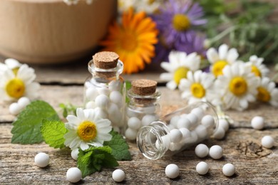 Homeopathic remedy. Many pills, bottles and chamomile flowers on wooden table, closeup