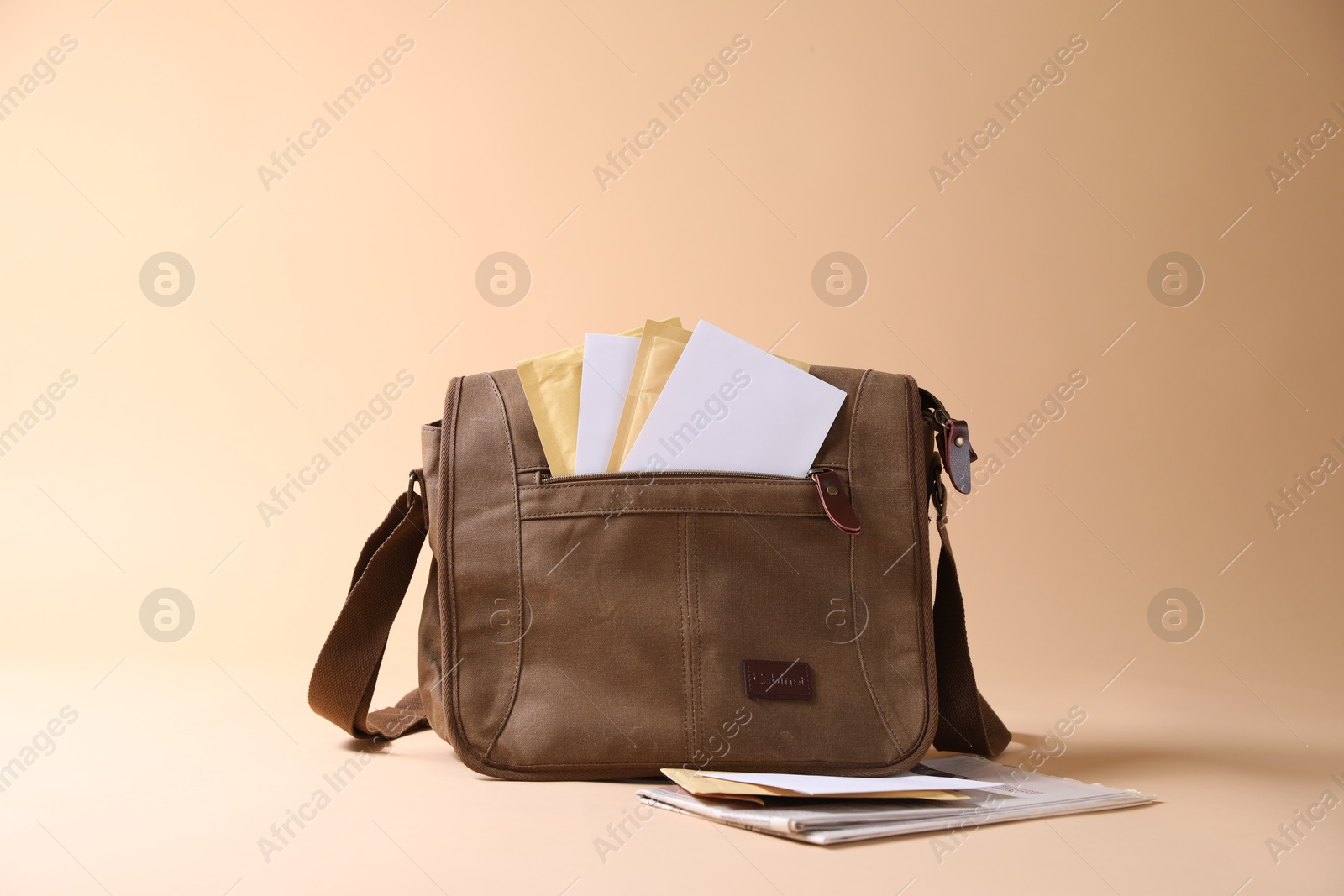 Photo of Brown postman's bag with envelopes and newspapers on beige background