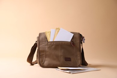 Photo of Brown postman's bag with envelopes and newspapers on beige background