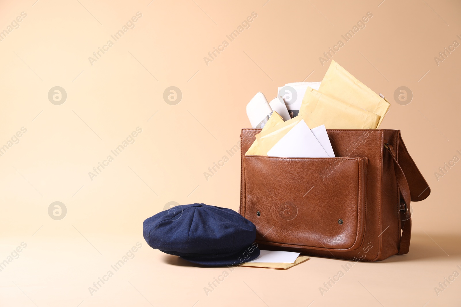 Photo of Brown postman's bag, envelopes, newspapers and hat on beige background. Space for text