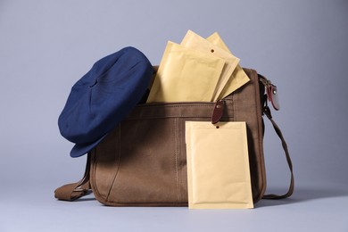 Brown postman's bag, envelopes, newspapers and hat on grey background