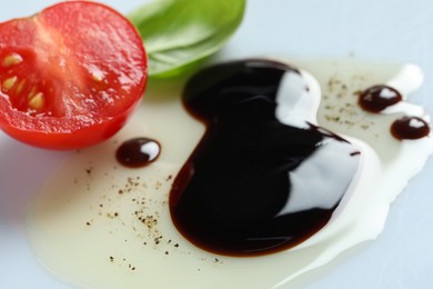 Photo of Delicious balsamic vinegar with olive oil, basil and cut tomato on white background, closeup