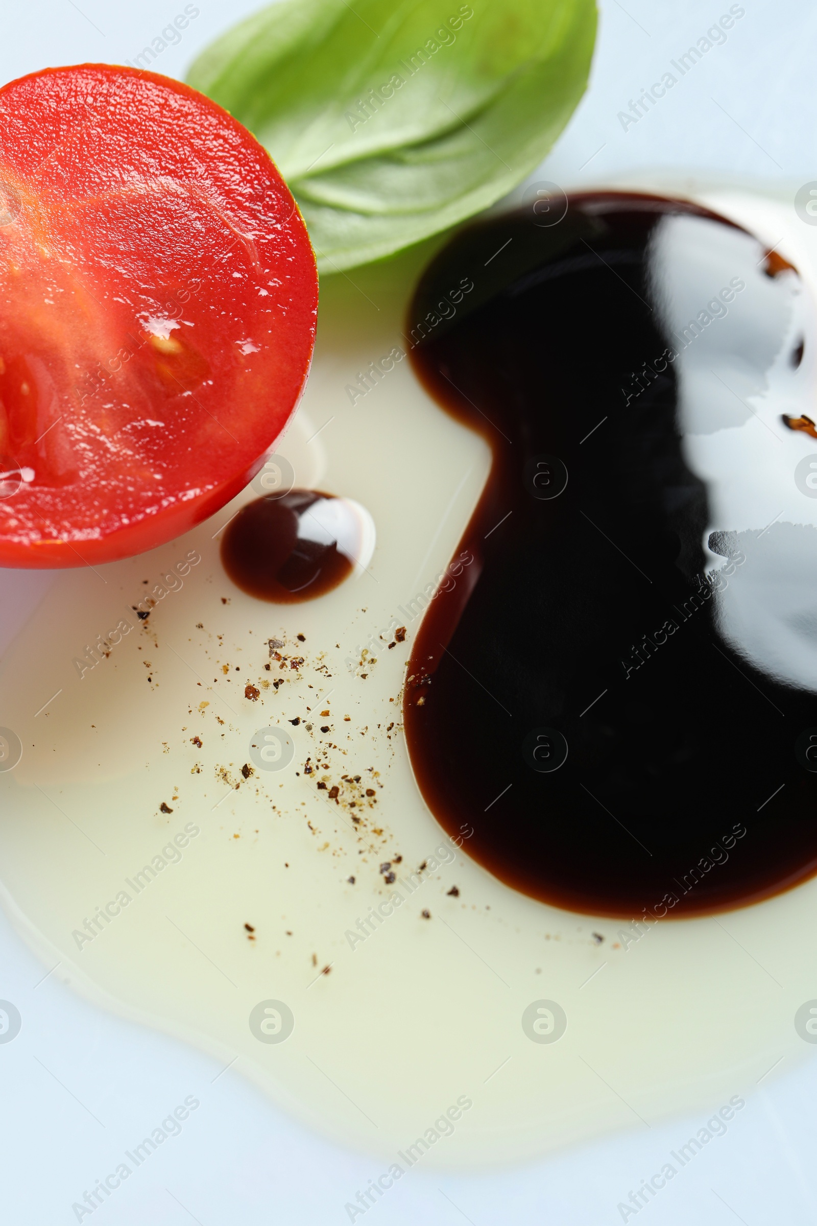 Photo of Delicious balsamic vinegar with olive oil, basil and cut tomato on white background, closeup