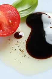 Photo of Delicious balsamic vinegar with olive oil, basil and cut tomato on white background, closeup