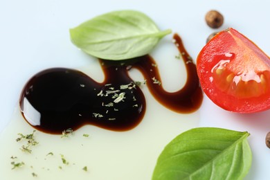 Delicious balsamic vinegar with olive oil, basil, tomato slice and peppercorns on white background, closeup