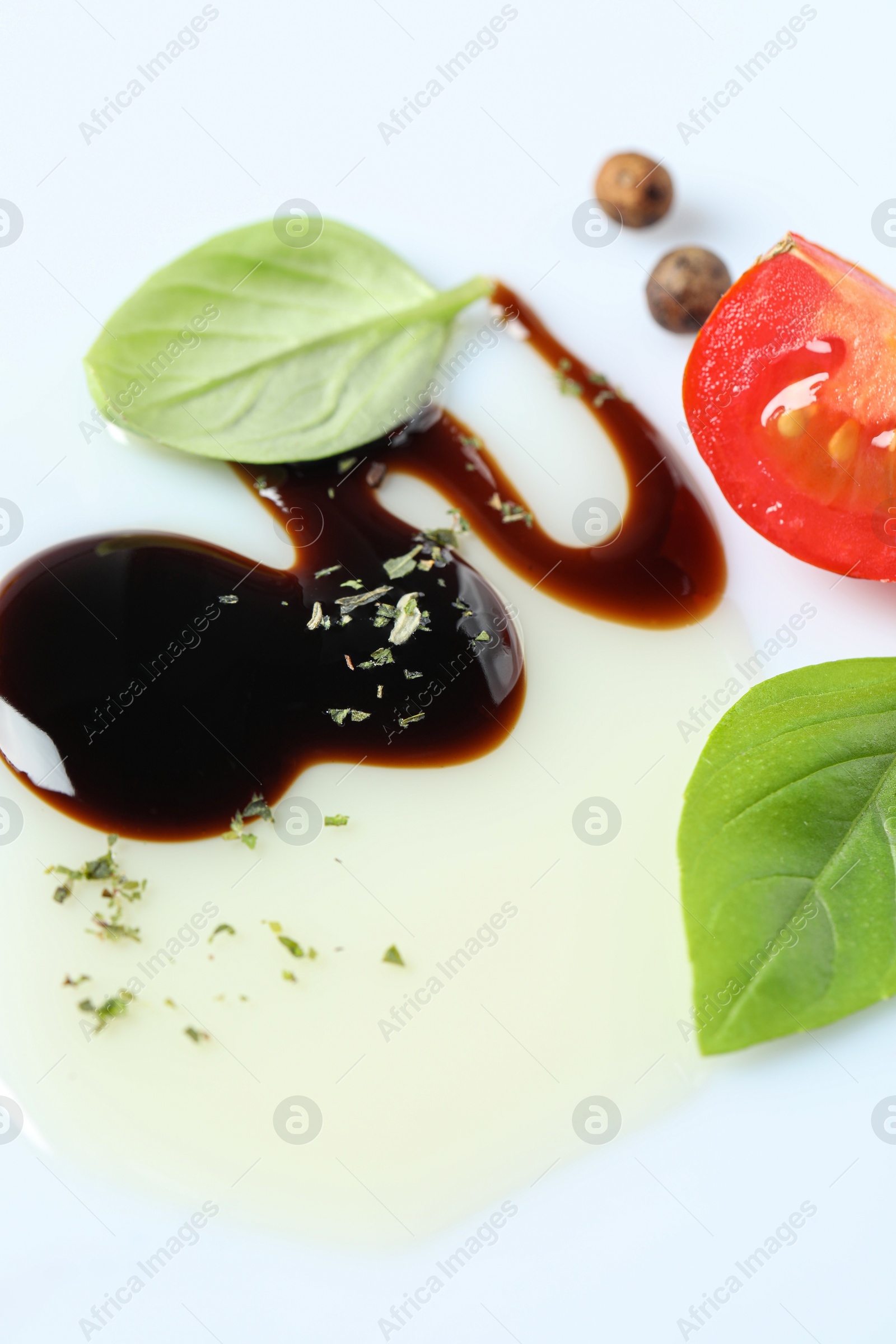 Photo of Delicious balsamic vinegar with olive oil, basil, tomato slice and peppercorns on white background, closeup