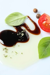 Delicious balsamic vinegar with olive oil, basil, tomato slice and peppercorns on white background, closeup