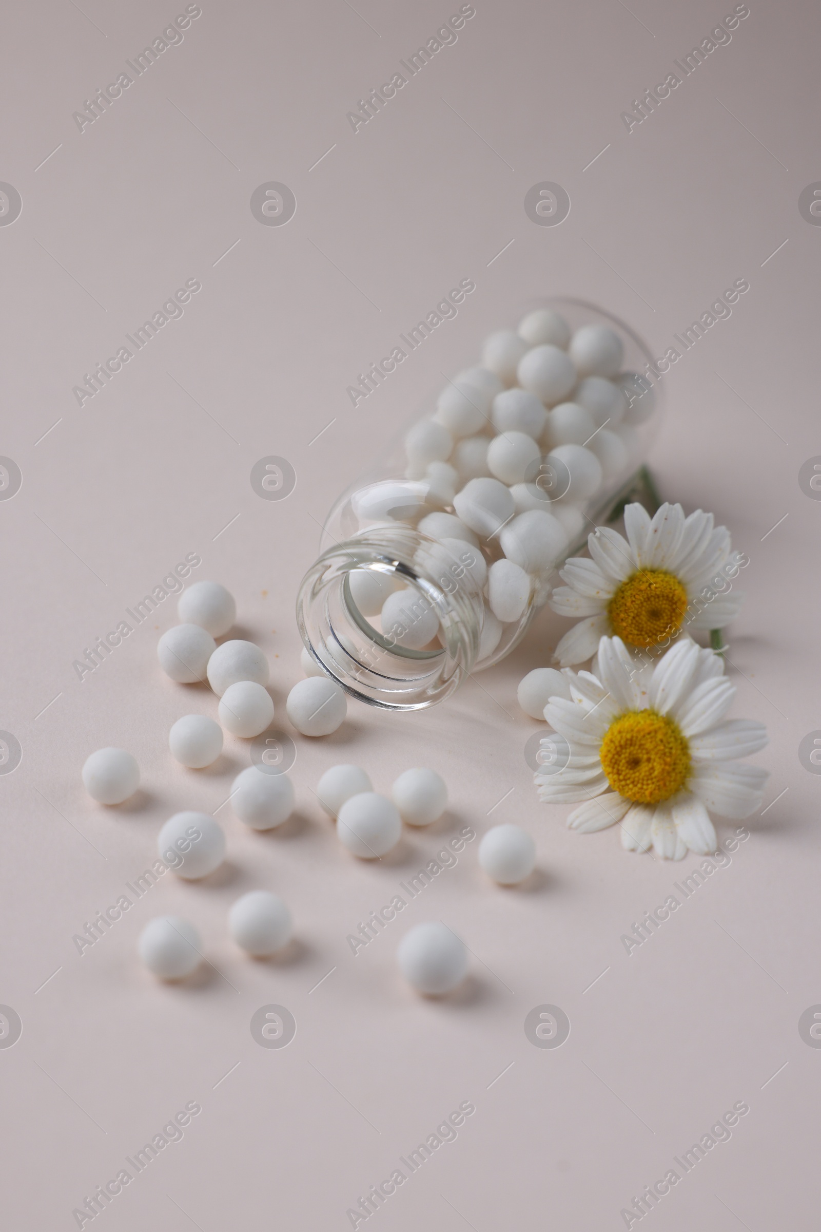 Photo of Homeopathy. Glass bottle, pills and chamomiles on beige background