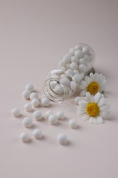 Homeopathy. Glass bottle, pills and chamomiles on beige background