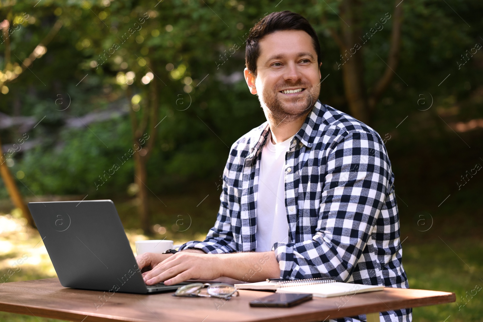 Photo of Smiling freelancer working with laptop at table outdoors. Remote job