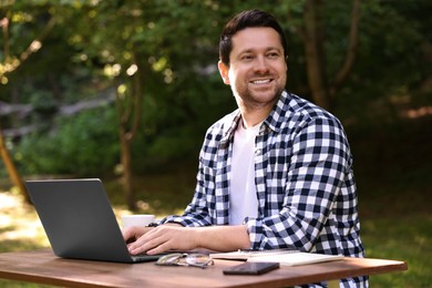 Smiling freelancer working with laptop at table outdoors. Remote job