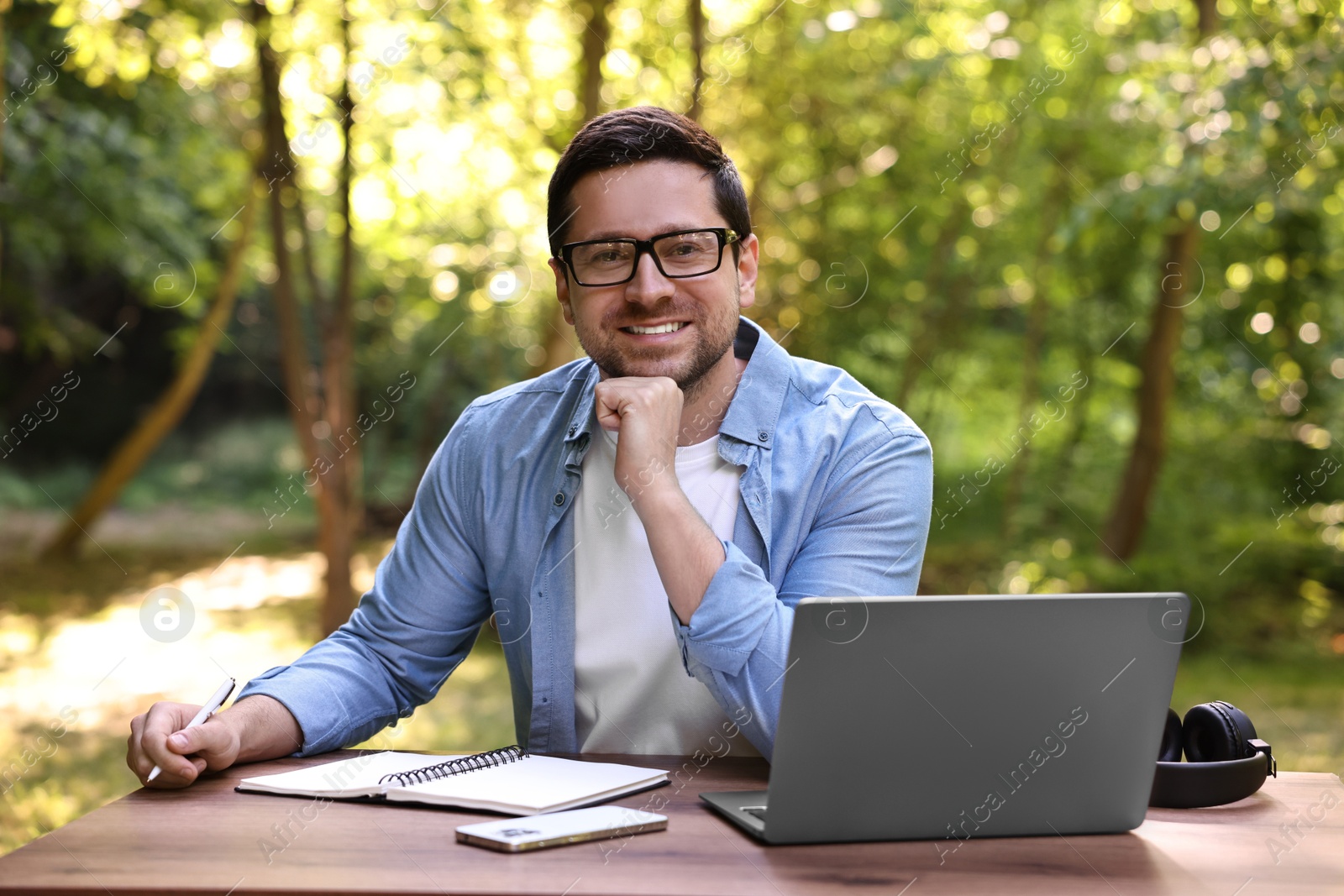 Photo of Smiling freelancer with laptop at table outdoors. Remote job