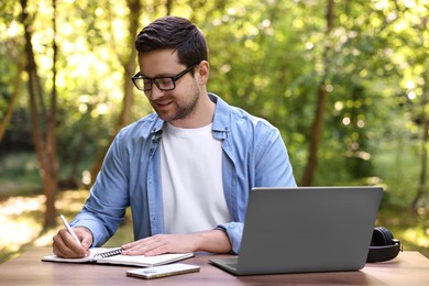 Smiling freelancer working with laptop and writing something at table outdoors. Remote job