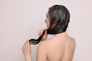 Woman applying hair mask on light background, back view