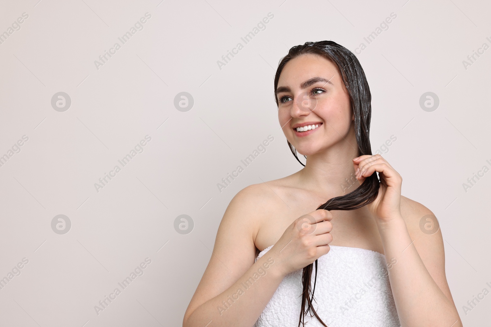 Photo of Smiling woman applying hair mask on light background. Space for text