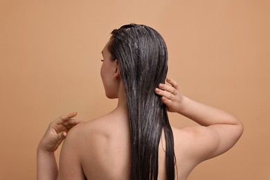 Woman applying hair mask on beige background, back view