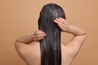 Woman applying hair mask on beige background, back view