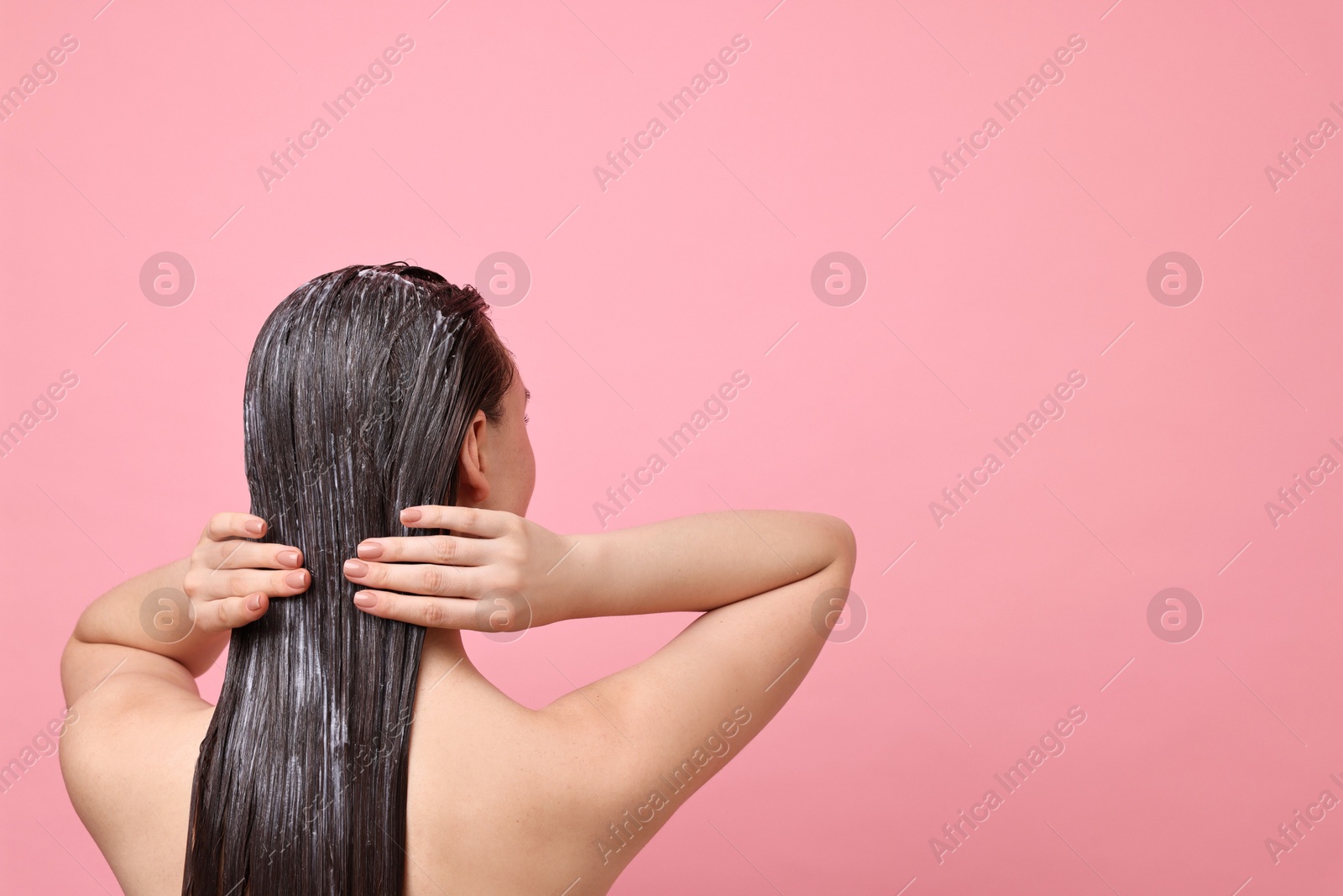 Photo of Woman applying hair mask on pink background, back view. Space for text