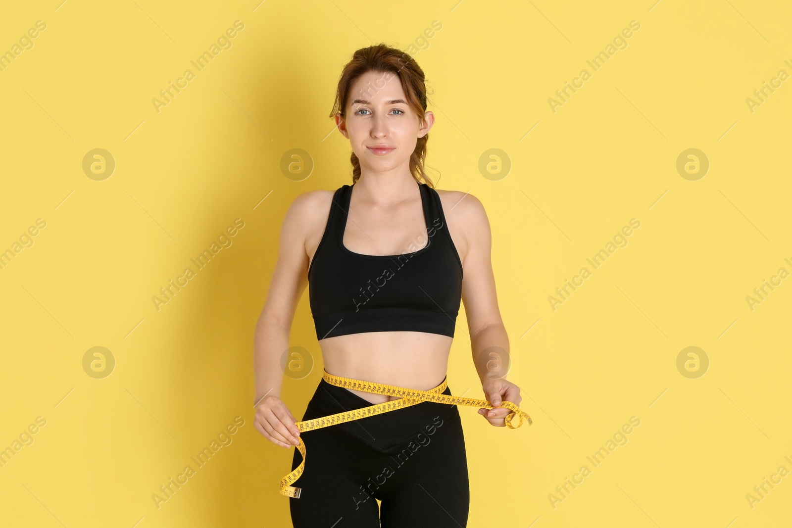 Photo of Woman with measuring tape showing her slim body against yellow background