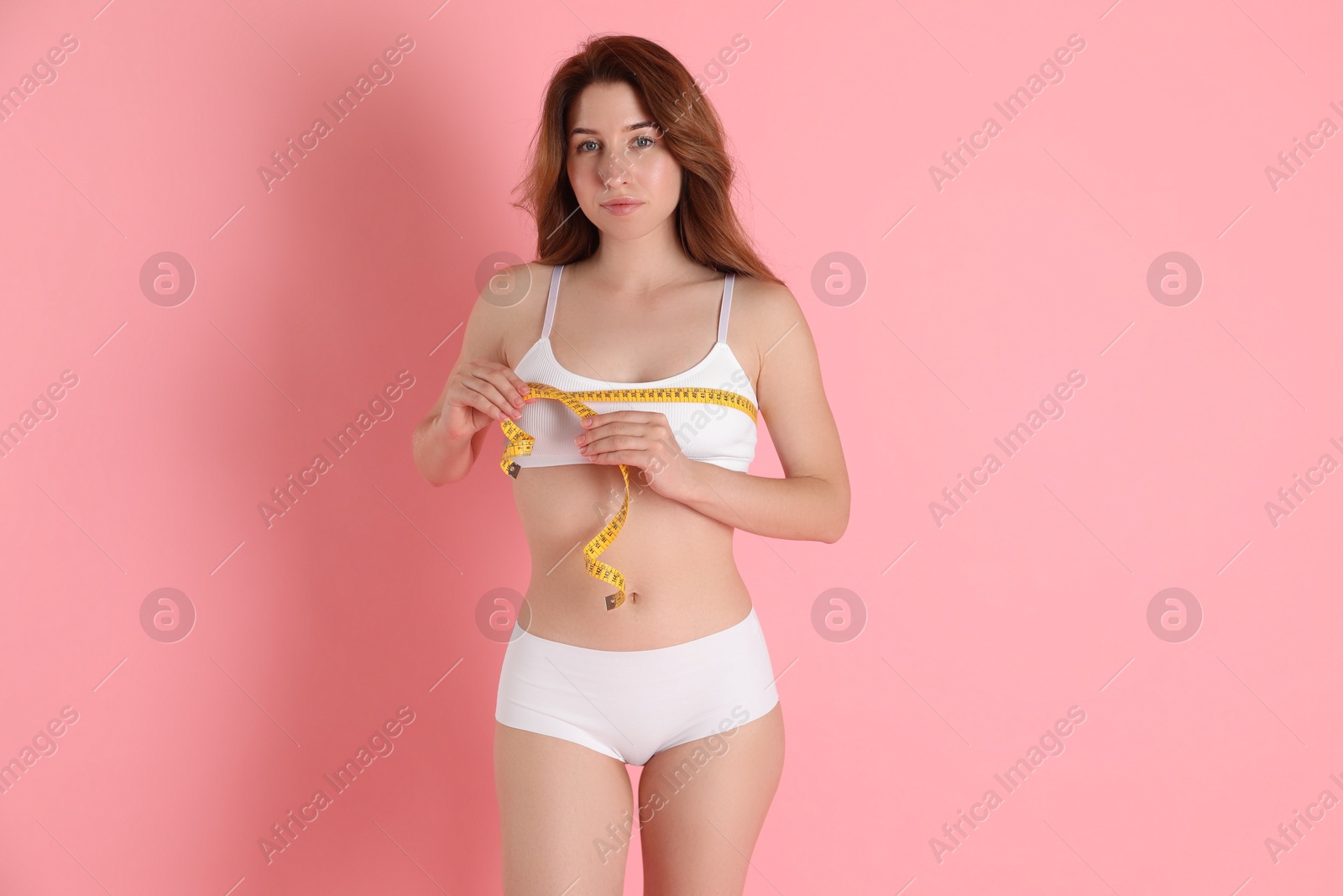 Photo of Woman with measuring tape showing her slim body against pink background