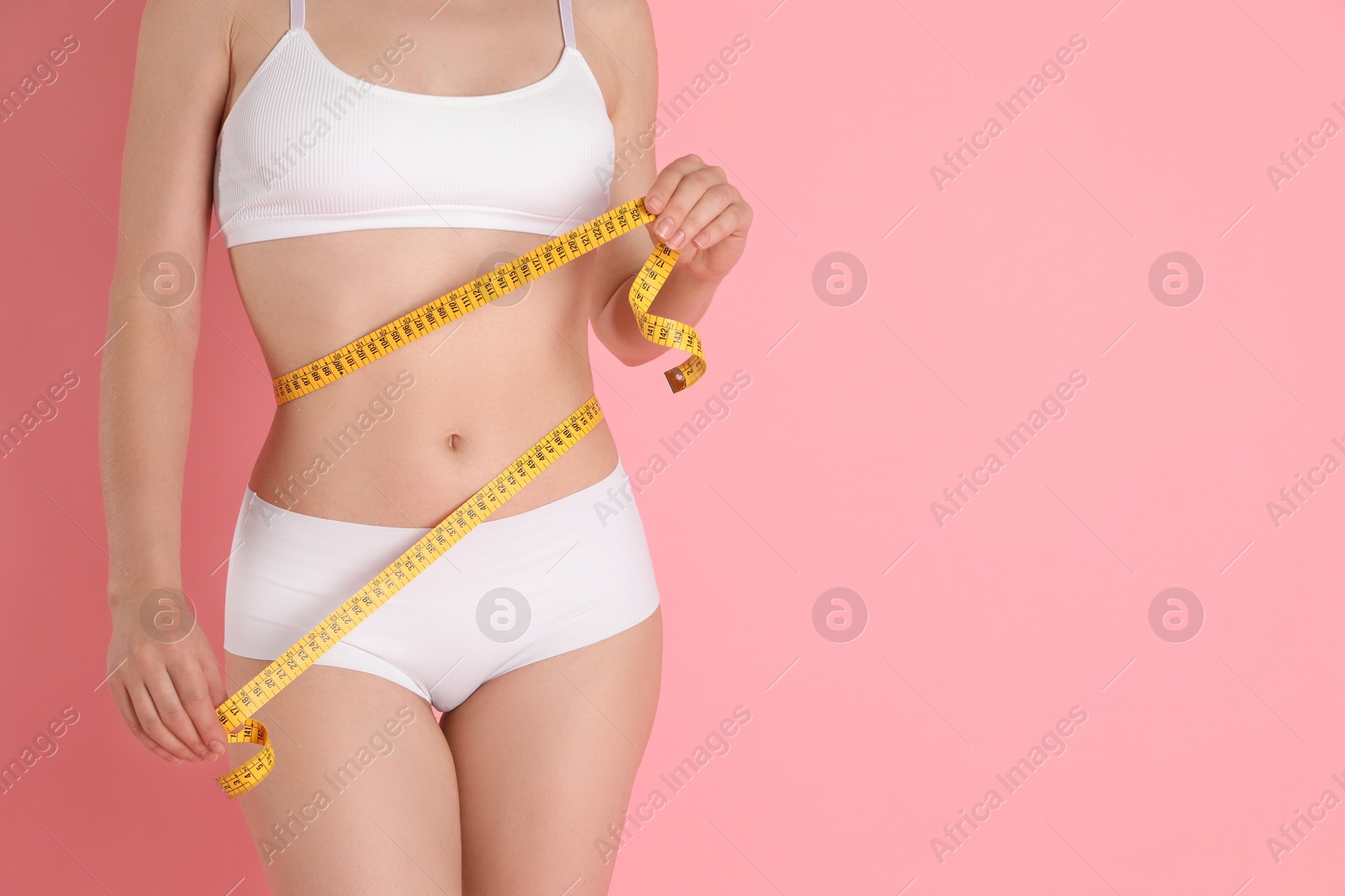 Photo of Woman with measuring tape showing her slim body against pink background, closeup. Space for text