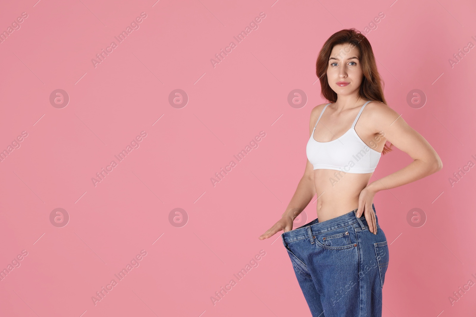 Photo of Woman in big jeans showing her slim body on pink background, space for text