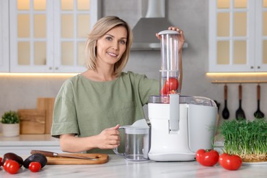 Smiling woman with fresh products using juicer at white marble table in kitchen