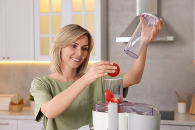 Photo of Smiling woman putting fresh tomato into juicer in kitchen