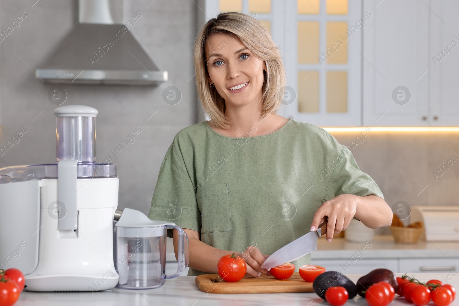 Photo of Juicer and fresh products on white marble table. Smiling woman cutting tomato in kitchen