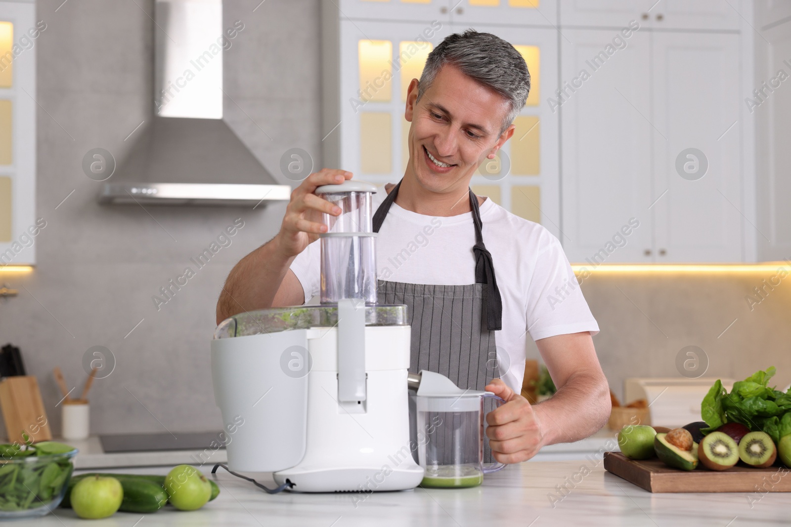 Photo of Smiling man with fresh products using juicer at white marble table in kitchen