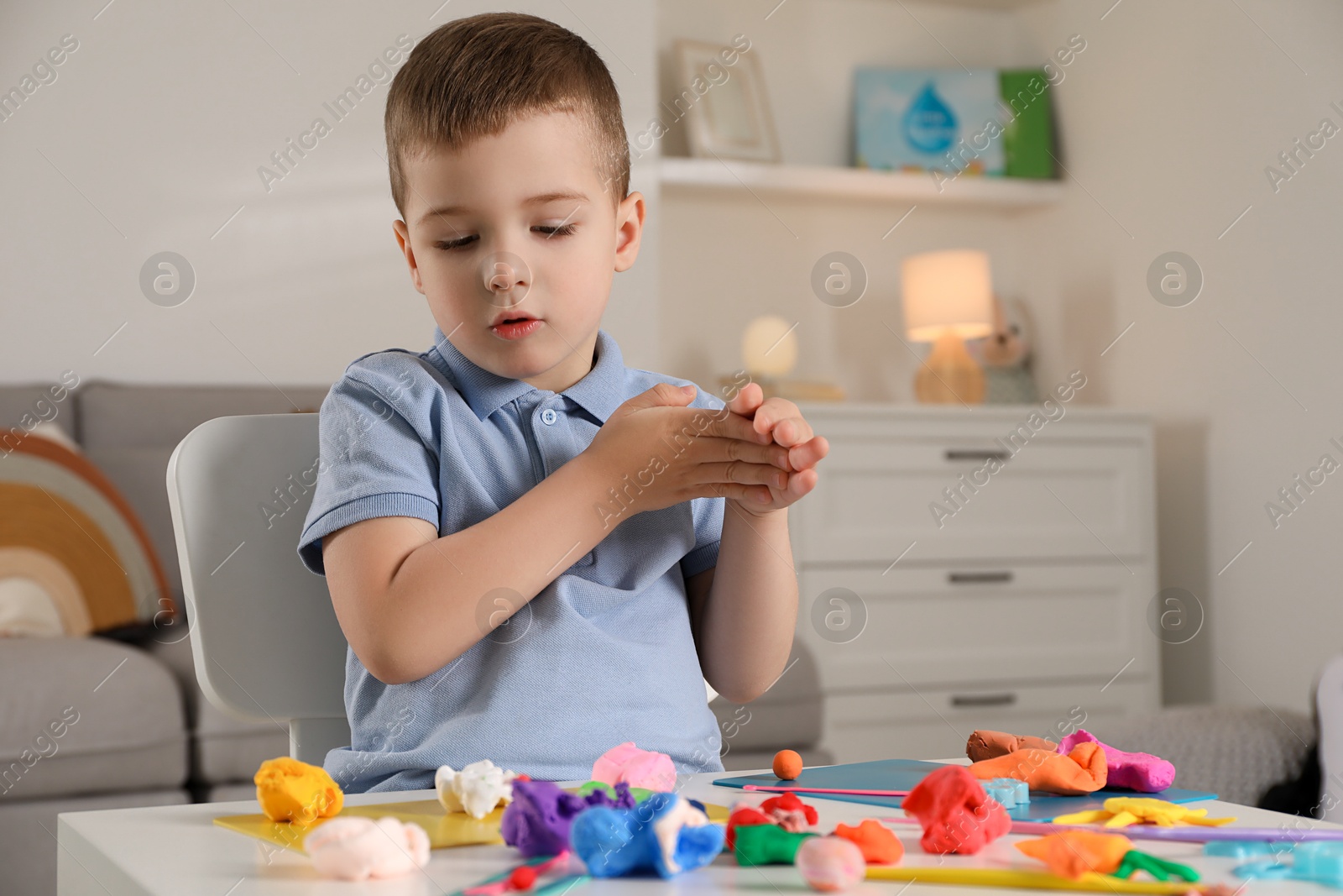 Photo of Little boy sculpting with play dough at table indoors