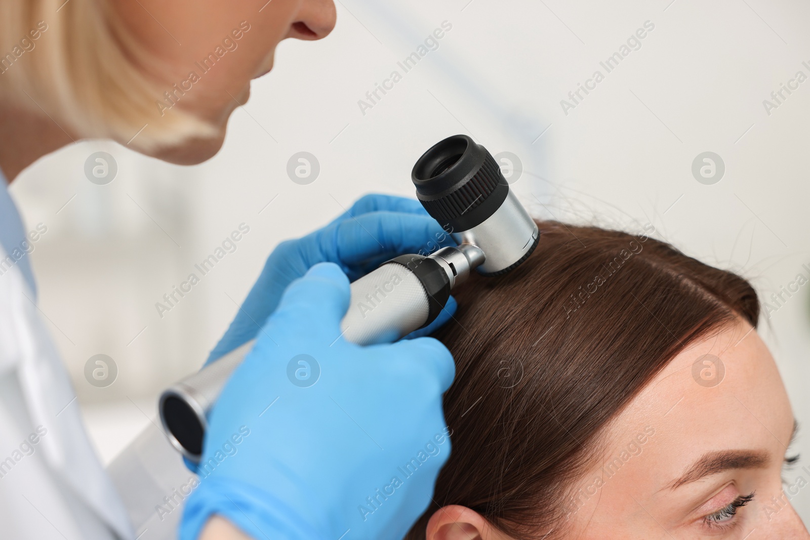 Photo of Trichologist with dermatoscope examining patient`s hair in clinic, closeup