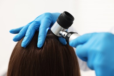 Photo of Trichologist with dermatoscope examining patient`s hair in clinic, closeup