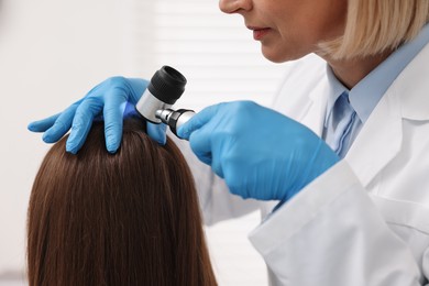 Trichologist with dermatoscope examining patient`s hair in clinic, closeup