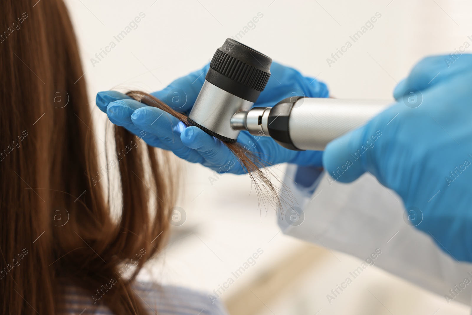 Photo of Trichologist with dermatoscope examining patient`s hair in clinic, closeup