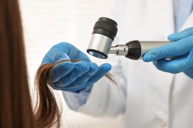 Photo of Trichologist with dermatoscope examining patient`s hair in clinic, closeup