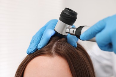 Trichologist with dermatoscope examining patient`s hair in clinic, closeup