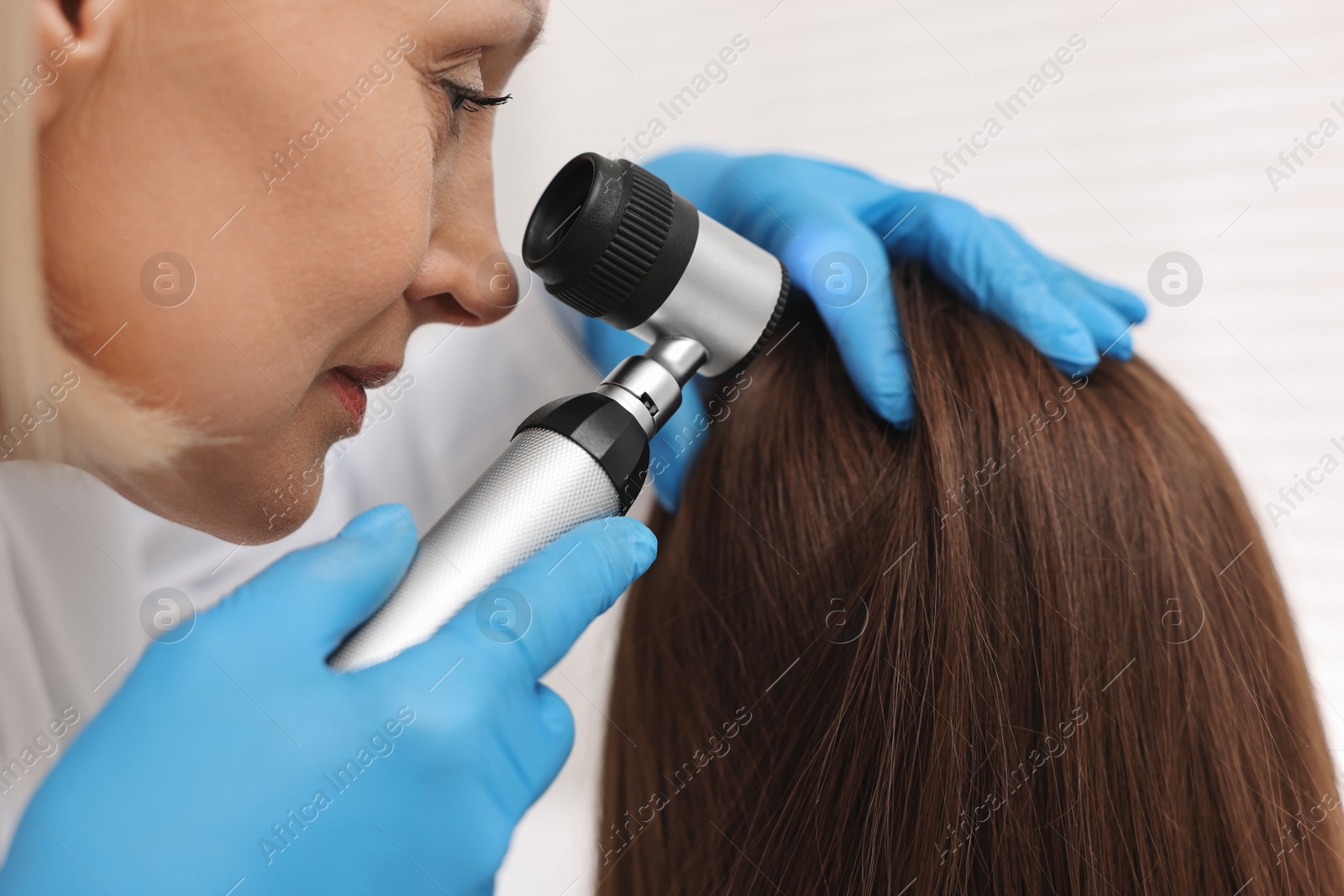 Photo of Trichologist with dermatoscope examining patient`s hair in clinic, closeup