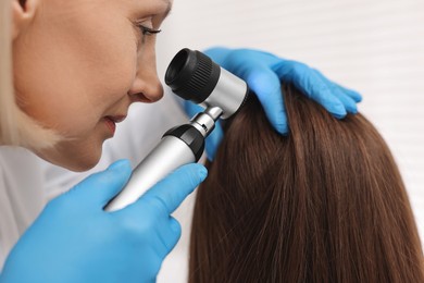 Photo of Trichologist with dermatoscope examining patient`s hair in clinic, closeup